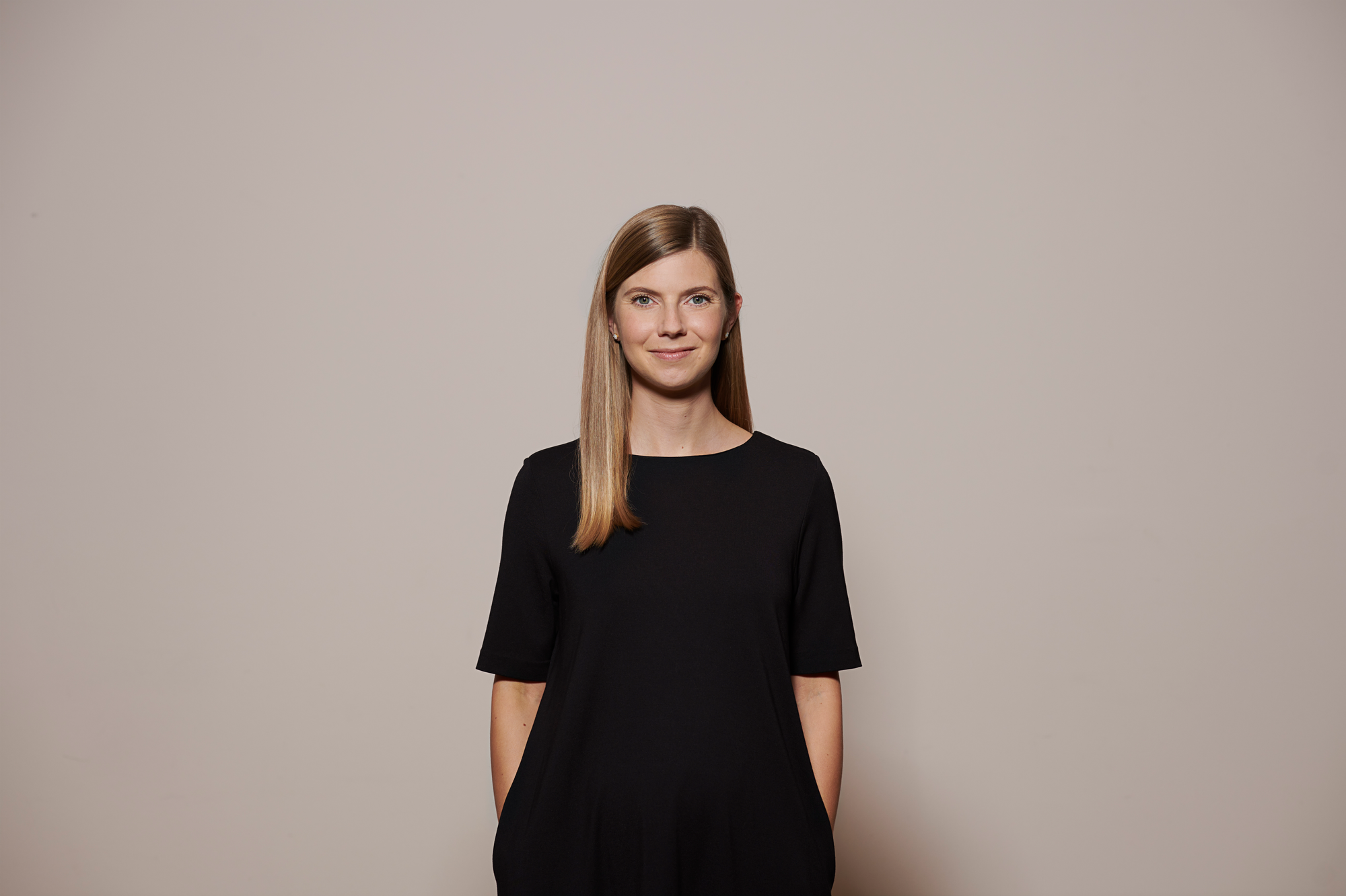 a picture of a woman in front of a white wall, wearing a black dress 