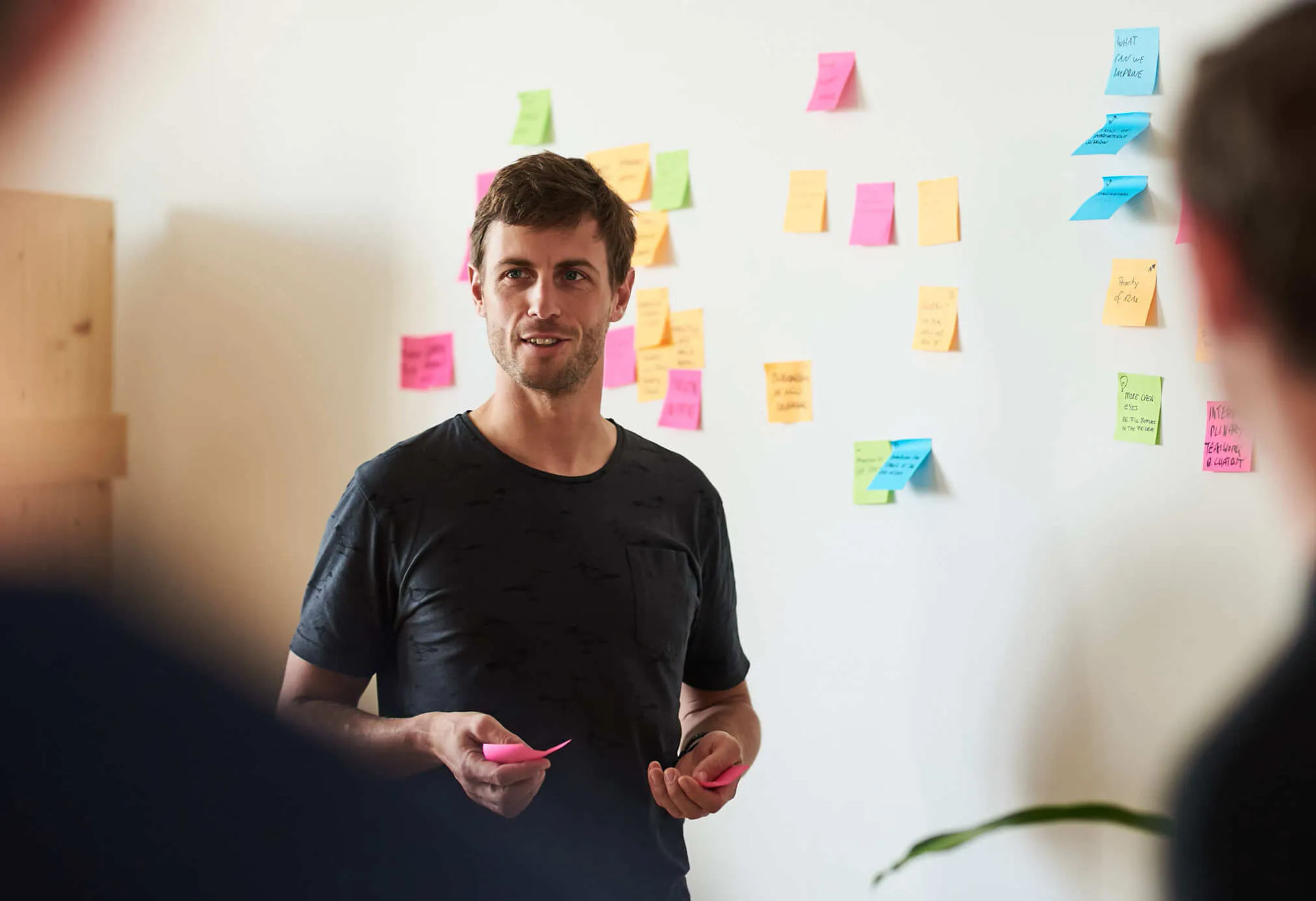 A man standing in front of a wall covered in colorful sticky notes, representing ideas and reminders.